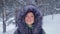 A young woman smiles in a hood in a winter park in a snowfall