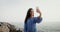 Young woman smiles while taking a selfie on a mobile standing on rocky sea coast