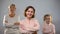 Young woman smiling on camera, child and senior lady behind, generations link