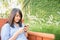 Young woman smiling and cell phone texting sitting on a park bench in autumn or fall.