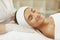 Young woman smiling with eyes closed lying on spa bed after skin care procedures