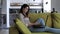 Young woman smilling sitting in cozy living room on green couch holding using laptop. Smiling casual lady chatting with