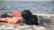 Young woman spitting water, lying near life jackets on shore, flood survivor