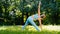 Young woman sportive trainer changes yoga positions stretching on green meadow grass