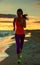 Young woman in sports gear on beach at sunset jogging