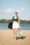 Young woman in sportswear, cap and skirt walking on beach with paddle tennis racket on warm, sunny day. Outdoors