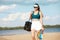Young woman in sportswear, cap and skirt walking on beach with paddle tennis racket on warm, sunny day. Outdoors