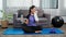 Young woman in sportswear is sitting on mat to prepare yoga exercise in the living room at home