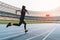 Young woman in sportswear sprinting on running track stadium at sunset