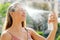Young woman spraying Thermal Water on her face outside. Thermal water used for skin care, fix makeup, help skin irritation,