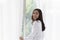 Young woman stand open white curtains at the window in morning after waking up in bedroom. Happy female opening window curtains at