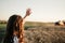 Young woman standing back on field and waving hand to a tractor driver in sunset