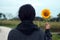 Young woman standing from the back holding sunflower plant blossom in hand. Still life concept.