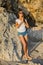 Young woman standing barefoot on the sand near the rock. Hands in namaste mudra. Caucasian woman wearing jeans shorts, white T-