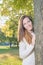 Young woman standing behind tree outdoor in park