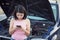 Young woman standing by broken car on the road and using smartphone calling assistance