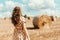 Young woman standing on harvested field with straw bales. Agriculture background with copy space. Summer and autumn harvest