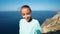 Young woman standing on high cliff edge over sea enjoying sunny summer morning