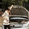 Young woman standing near the broken car. The girl opened the hood and look at the engine. Refit woman car