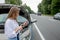 Young woman standing near broken down car with popped up hood having trouble with her vehicle. Waiting for help tow truck or