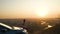 Young woman standing near her car enjoying warm sunset view. Girl traveler leaning on vehicle hood looking at evening horizon.