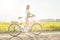 Young woman standing next to her electric bike over dusty country road, strong afternoon sun backlight in background shines on