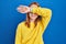 Young woman standing over blue background covering eyes with arm, looking serious and sad