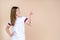 Young woman standing on pastel beige background and pointing fingers away