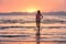 Young woman standing in sea with waves at sunset