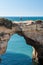 A young woman standing and waving on Natural arch above ocean, Arco de Albandeira, Algarve, Portugal. Stone arch at Praia de