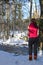 Young woman standing in wintry forest and watching a creek.