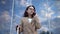 A young woman stands against the background of a business center and speaks on the phone. Girl in a coat with a suitcase