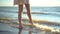 A young woman stands barefoot on the sandy seashore. The girl wets her feet close-up.