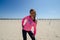 Young woman stands on the beach, wearing a neon pink YOLO shirt with sunglasses, as her hair blows in the wind