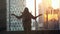 Young woman stands by the big window stretches arms and hair and looking out her apartment on the city buildings during