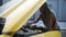 Young woman stands near yellow car with opened bonnet and repairs it