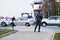 A young woman stands at a pedestrian crossing. Heavy traffic on road