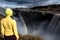 A young woman stands on the shore of the falling water of the most powerful waterfall in Europe - Dettifoss. Colorful summer day i