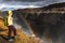 A young woman stands on the shore of the falling water of the most powerful waterfall in Europe - Dettifoss. Colorful summer day i