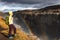 A young woman stands on the shore of the falling water of the most powerful waterfall in Europe - Dettifoss. Colorful summer day i