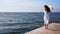 Young woman stands on wooden pier, looking at the sea.