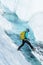 Young woman stepping over a crevasse filled with deep blue water from the melting ice of the Matanuska Glacier