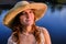 A young woman in a straw hat on the background of a pond in the sunset rays