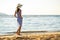 Young woman in straw hat and a dress walking alone on empty sand beach at sea shore. Lonely tourist girl looking at horizon over