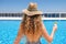 Young woman in straw hat holding sun protection cream suntan sunscreen lotion near swimming pool at resort