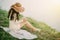 Young woman in a straw hat with long hair sits on the shore of the lake on the grass and writes a letter. concept of romance