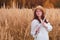 A young woman in straw hat with red hair plays a flute in an autumn field. A musician with a wind instrument in the tall grass