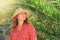 A young woman in a straw hat stands under a fern branch. Tourist in tropical country, sun and nature