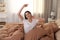 Young woman stretching on bed with brown linens at home