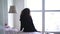 Young woman stretching on bed in front of big window. Back view of brunette caucasian girl in pajamas waking up in